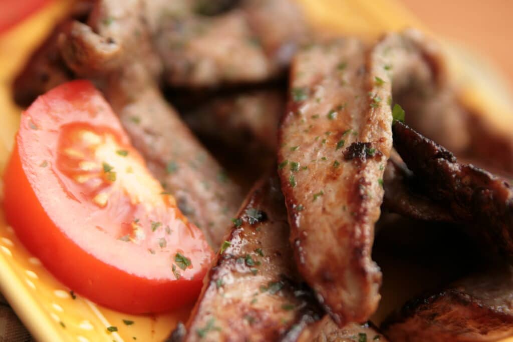 Viande Grillée Persillade et Tomate Fraîche Tranches de viande grillée et assaisonnée de persil, servies avec une tranche de tomate juteuse sur une assiette jaune vif.