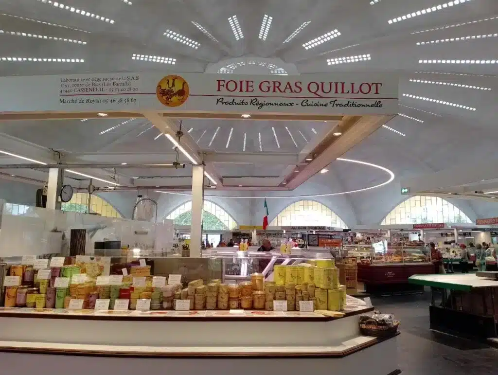 Foie Gras Quillot : Produits Régionaux au Marché de Royan Intérieur du marché couvert avec un stand de Foie Gras Quillot proposant des produits régionaux sous un plafond voûté lumineux. Texte visible : FOIE GRAS QUILLOT.