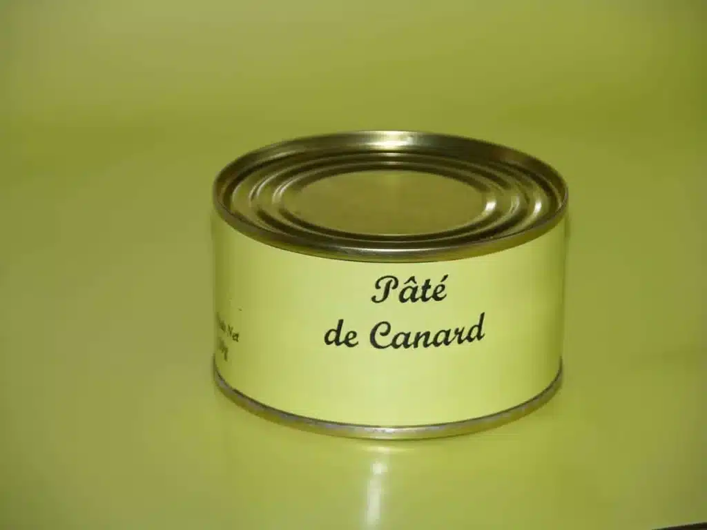 Pâté de Canard en Conserve : Délice Français Conserve de Pâté de Canard avec étiquette jaune clair, posée sur une surface réfléchissante vert anis.